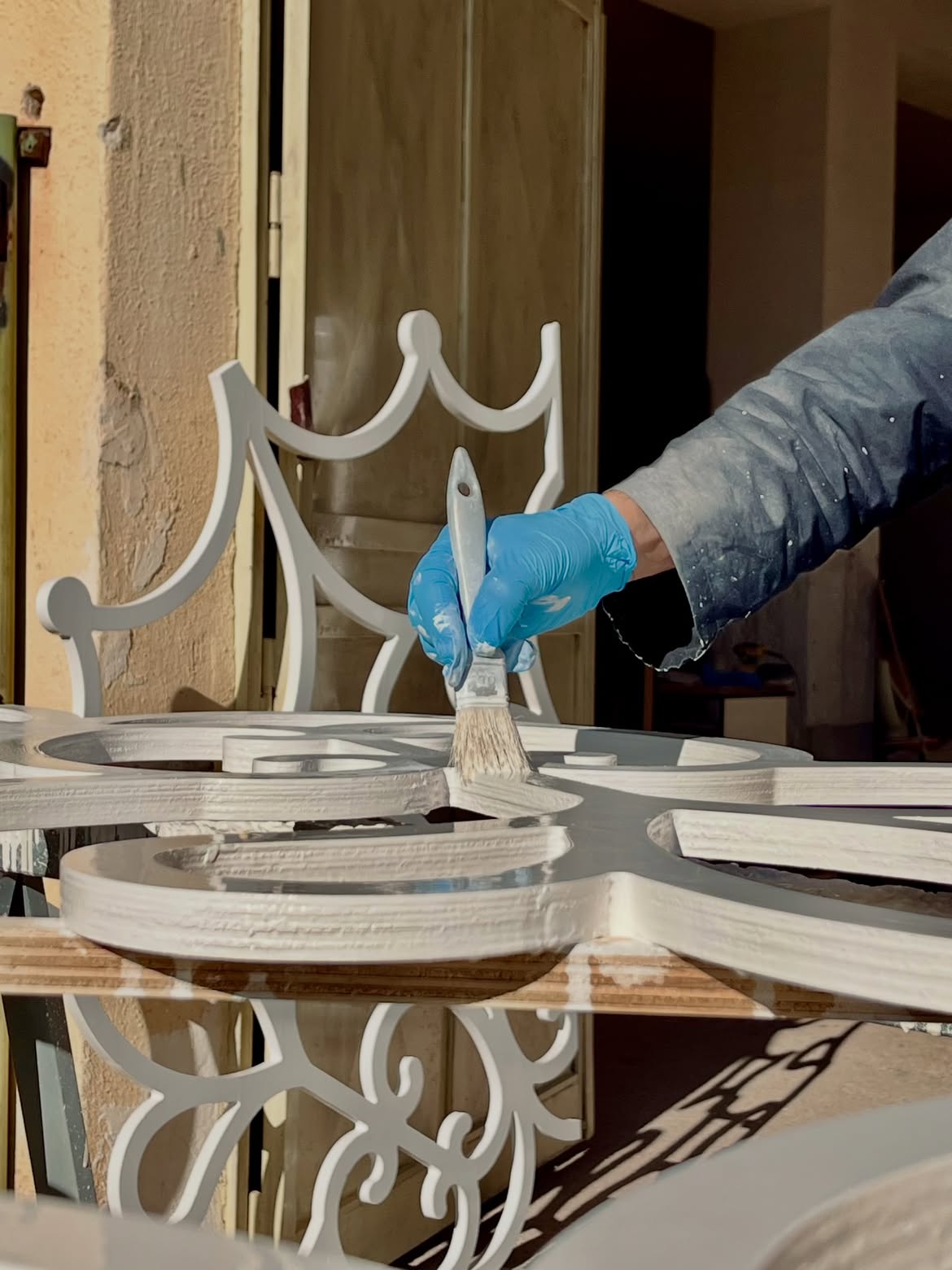 A maker's hand painting a white wooden luminaria frame in a Salento workshop